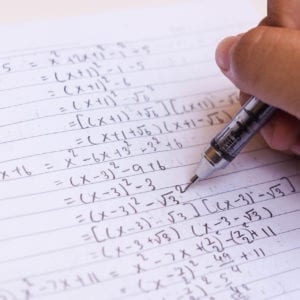 student writing algebra equations on paper