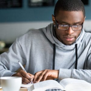 college age african american man writing notes at coffee shop