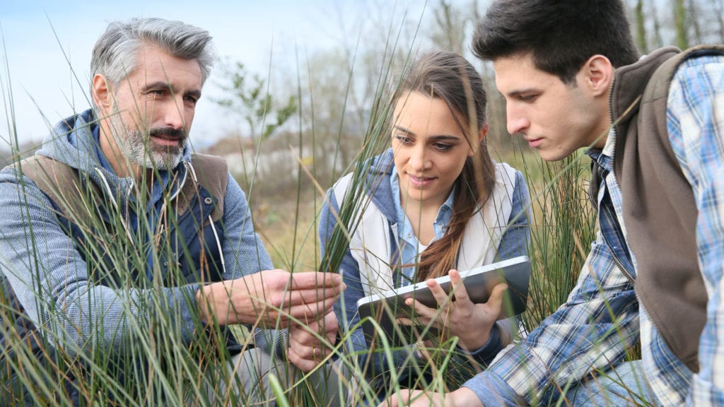 two students and teacher looking at grass samples