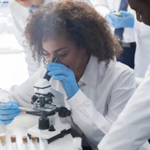 african american female college student looking into microscope in science lab